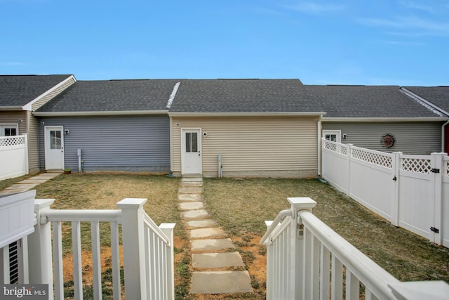 exterior space with a fenced backyard, a gate, a lawn, and roof with shingles