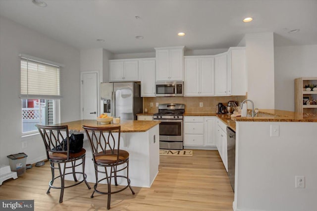 kitchen featuring tasteful backsplash, light wood-style flooring, stainless steel appliances, white cabinetry, and recessed lighting