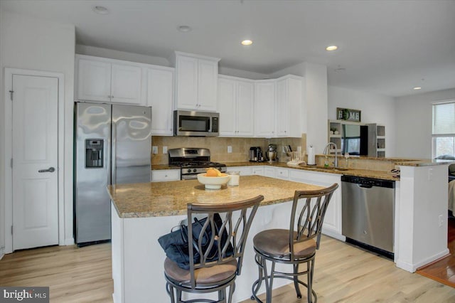 kitchen with a peninsula, a sink, stainless steel appliances, light wood-style floors, and backsplash