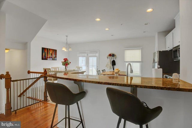 kitchen featuring a breakfast bar area, stainless steel appliances, white cabinetry, a healthy amount of sunlight, and light wood finished floors