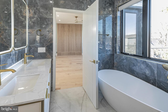 full bath with double vanity, a sink, marble finish floor, a freestanding bath, and tile walls