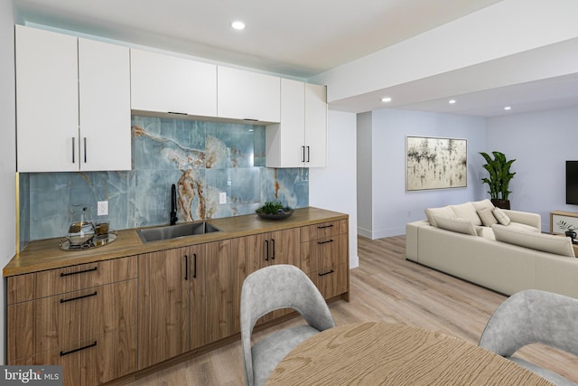 kitchen with a sink, white cabinetry, open floor plan, light wood-type flooring, and backsplash