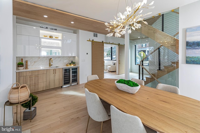 dining room featuring a barn door, beverage cooler, light wood-style floors, stairs, and indoor wet bar