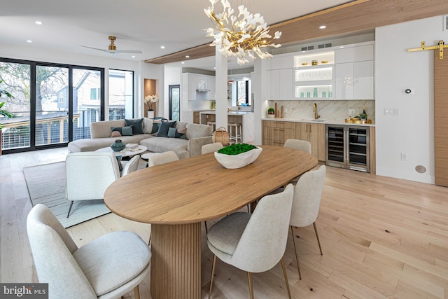 dining room with a notable chandelier, recessed lighting, light wood-style floors, wet bar, and beverage cooler