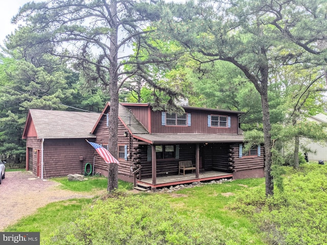 view of front of house with a porch, log exterior, driveway, and a front lawn