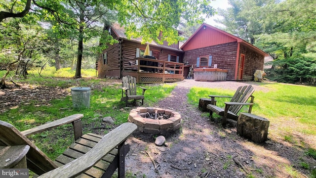 rear view of house with log siding, a fire pit, a wooden deck, and a lawn