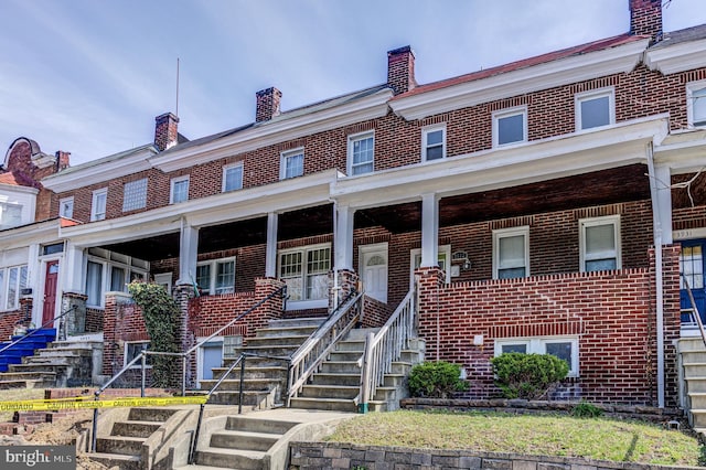 multi unit property with brick siding, covered porch, and a chimney