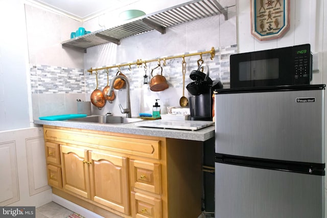 kitchen with black microwave, a sink, light countertops, stainless steel refrigerator, and decorative backsplash