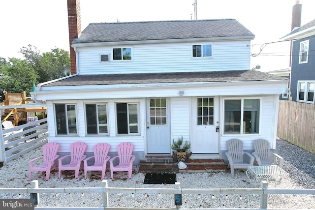 rear view of house featuring roof with shingles, a chimney, and fence