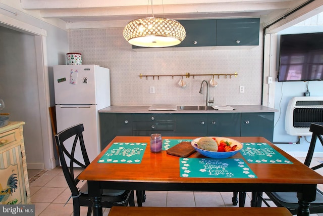 kitchen with light tile patterned floors, beamed ceiling, freestanding refrigerator, heating unit, and a sink