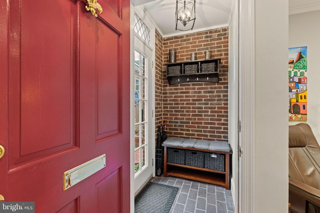 mudroom with a chandelier, brick wall, crown molding, and brick floor