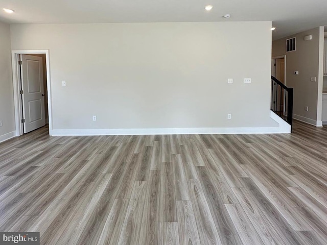 unfurnished room with light wood-style floors, visible vents, stairway, and baseboards