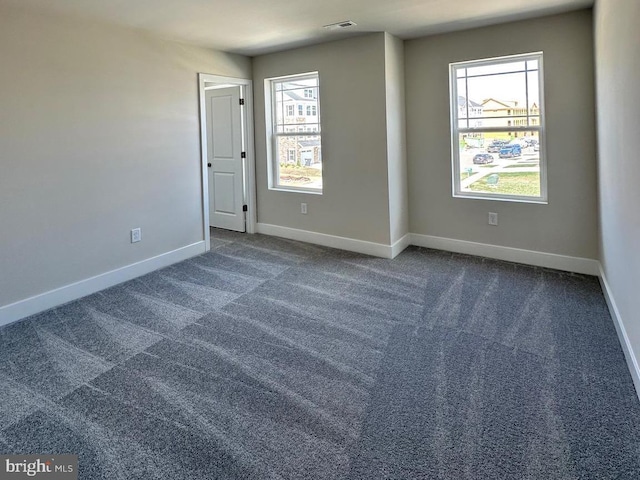 empty room with a wealth of natural light, baseboards, and dark colored carpet