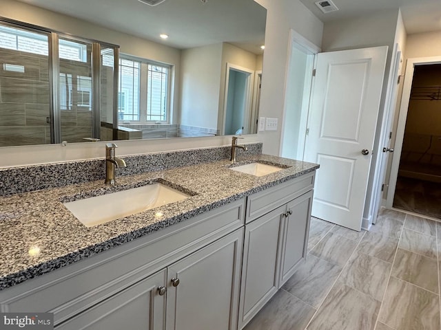 bathroom with double vanity, a stall shower, a spacious closet, and a sink