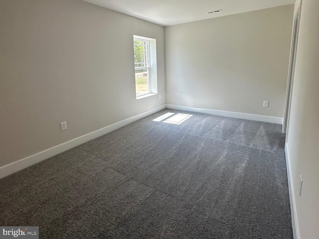 spare room with dark colored carpet, visible vents, and baseboards