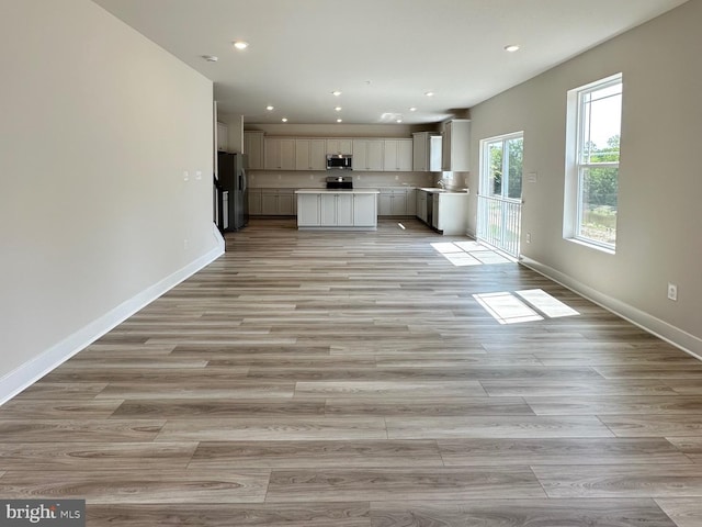 kitchen featuring stainless steel appliances, light countertops, light wood-style flooring, open floor plan, and baseboards