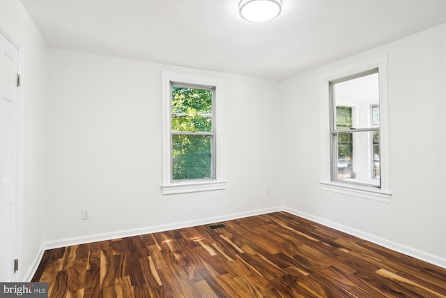 empty room featuring dark wood-style floors, a healthy amount of sunlight, visible vents, and baseboards