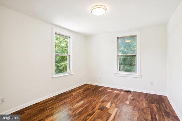 spare room featuring dark wood-style floors, visible vents, and baseboards