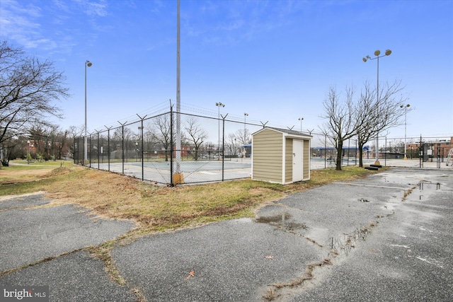 exterior space with a tennis court, fence, and an outdoor structure