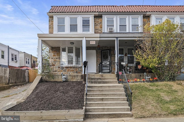 view of front of home with stone siding, covered porch, fence, and a tiled roof