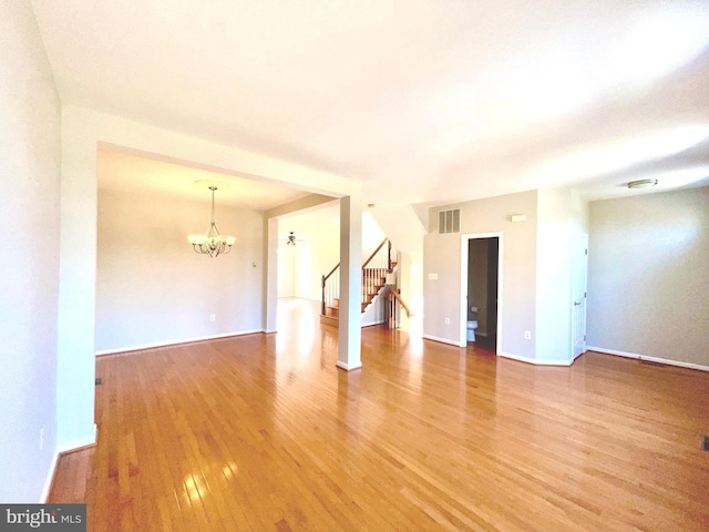 unfurnished room featuring baseboards, visible vents, light wood-style flooring, stairs, and a chandelier