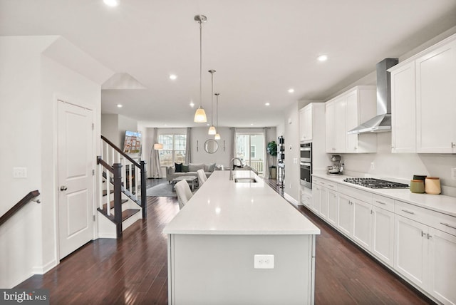 kitchen featuring wall chimney range hood, open floor plan, dark wood-style floors, stainless steel appliances, and a sink