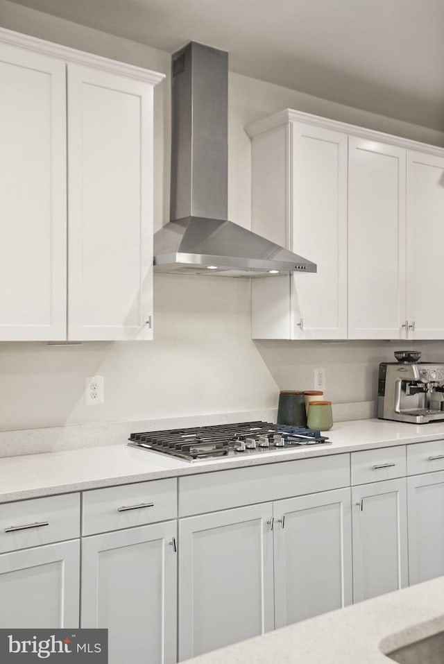 kitchen featuring light countertops, wall chimney range hood, white cabinets, and stainless steel gas stovetop