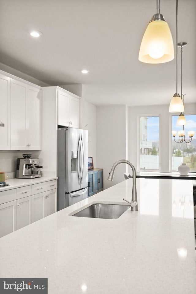 kitchen with recessed lighting, stainless steel refrigerator with ice dispenser, hanging light fixtures, white cabinets, and a sink