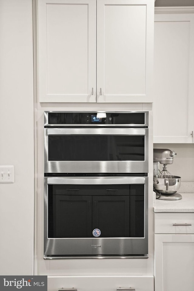 details with stainless steel double oven, light countertops, and white cabinetry