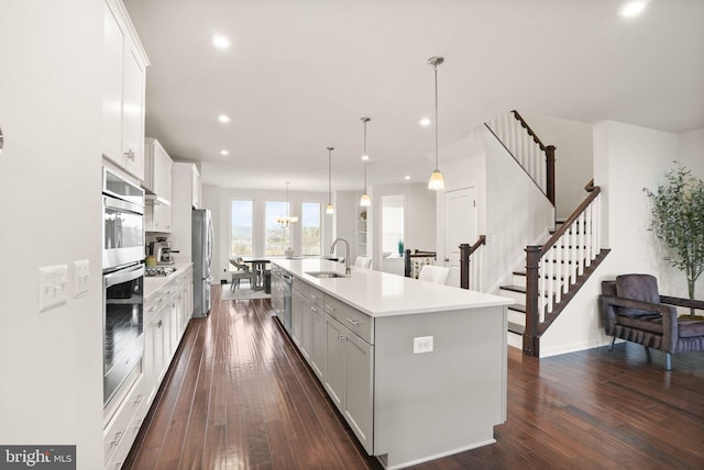 kitchen featuring a kitchen island with sink, a sink, appliances with stainless steel finishes, light countertops, and dark wood-style flooring