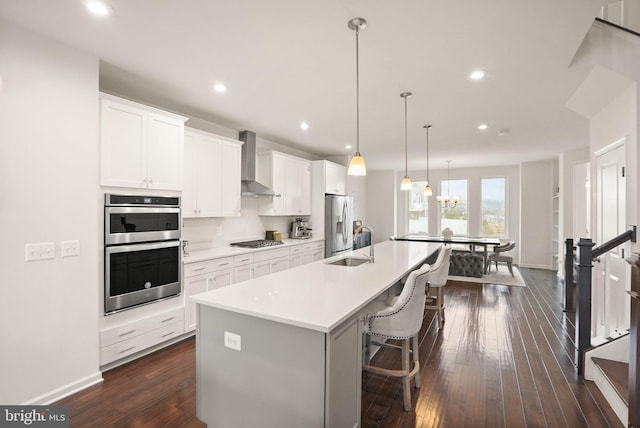 kitchen featuring a large island, a sink, stainless steel appliances, wall chimney range hood, and dark wood-style flooring