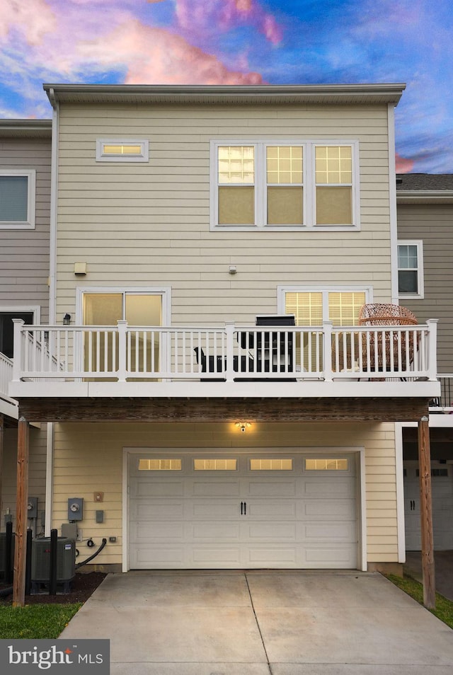 back of property at dusk featuring cooling unit, an attached garage, and driveway