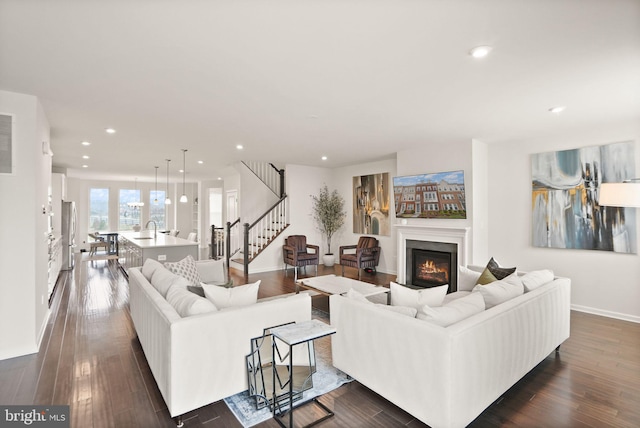 living area featuring a glass covered fireplace, stairway, dark wood finished floors, and recessed lighting