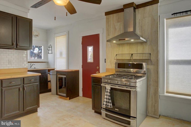 kitchen with ceiling fan, wall chimney range hood, backsplash, and stainless steel gas range oven