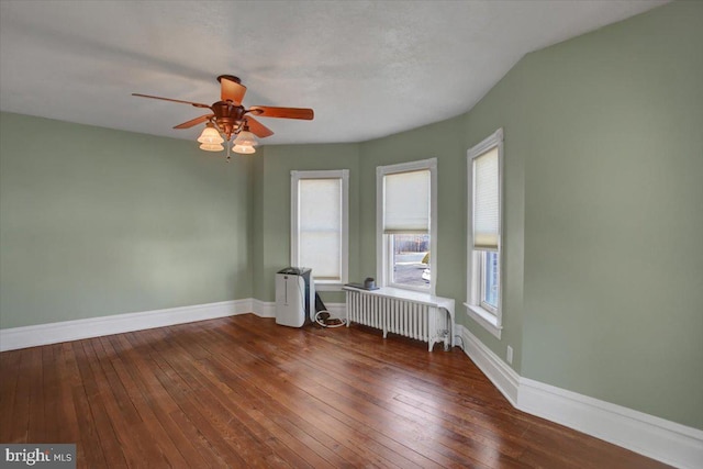 spare room featuring hardwood / wood-style floors, radiator heating unit, a ceiling fan, and baseboards