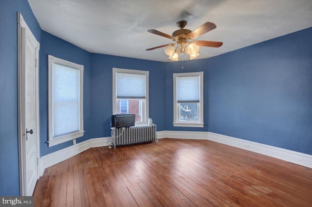 empty room with baseboards, radiator, ceiling fan, and hardwood / wood-style flooring