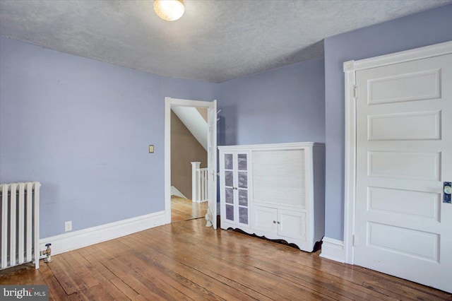 unfurnished bedroom featuring radiator, baseboards, and wood-type flooring