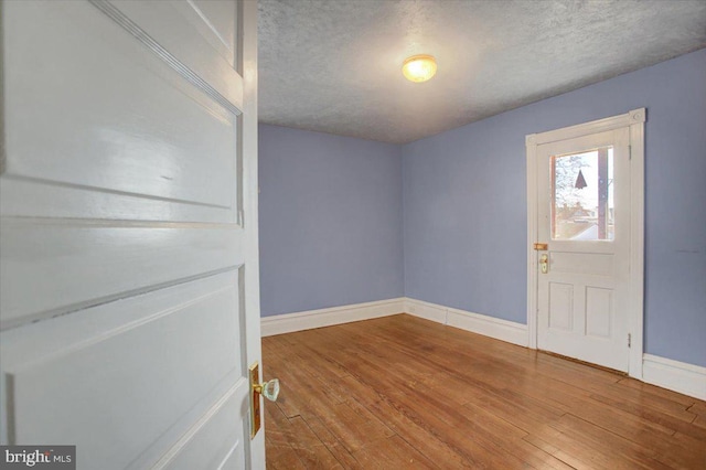 spare room featuring baseboards, a textured ceiling, and hardwood / wood-style floors