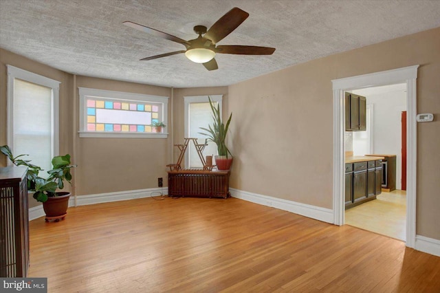 sitting room with baseboards, radiator heating unit, ceiling fan, a textured ceiling, and light wood-type flooring