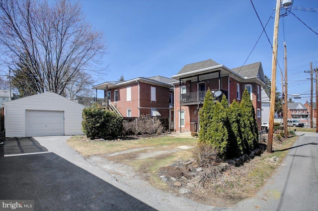 view of front of house featuring an outbuilding, driveway, a balcony, a garage, and brick siding