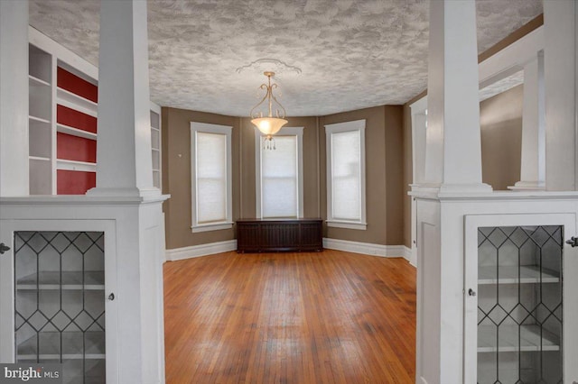 unfurnished living room with baseboards, a fireplace, hardwood / wood-style flooring, a textured ceiling, and ornate columns