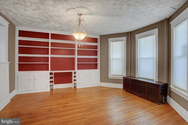 spare room with baseboards, a textured ceiling, hardwood / wood-style floors, and radiator heating unit