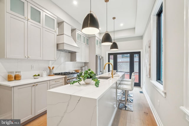 kitchen with stainless steel stove, a sink, light wood-style floors, a center island with sink, and custom range hood