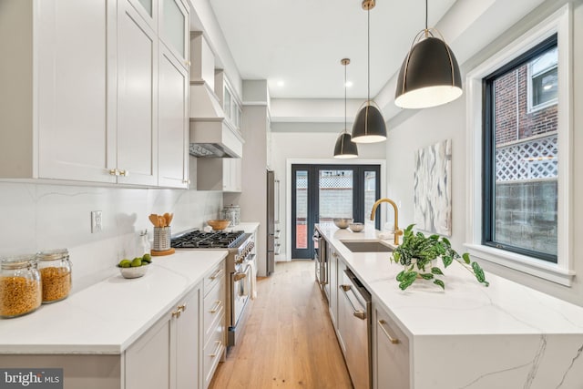 kitchen featuring custom exhaust hood, light wood-style flooring, appliances with stainless steel finishes, a sink, and a large island with sink