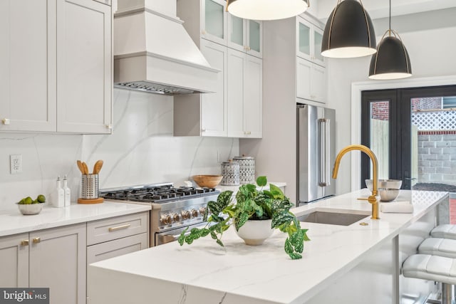 kitchen with light stone counters, high quality appliances, backsplash, custom exhaust hood, and decorative light fixtures