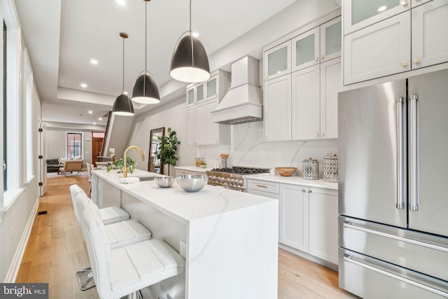 kitchen featuring light stone counters, premium range hood, stove, high end refrigerator, and light wood-style floors