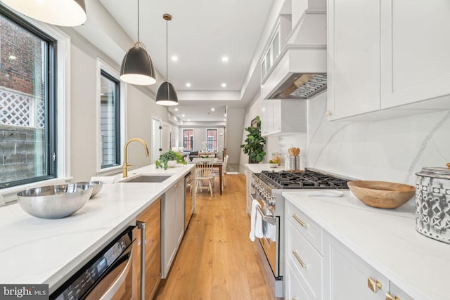 kitchen with appliances with stainless steel finishes, light stone countertops, custom exhaust hood, light wood-type flooring, and white cabinetry