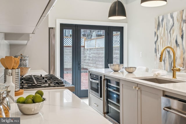 kitchen with beverage cooler, oven, light stone countertops, pendant lighting, and a sink