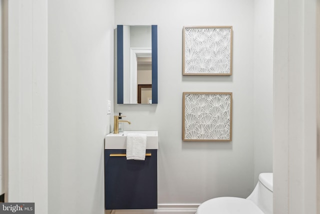 half bath featuring toilet, baseboards, and vanity