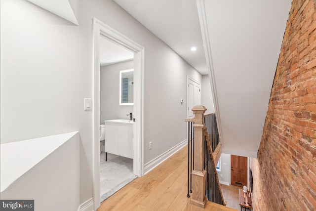 hall featuring brick wall, baseboards, an upstairs landing, and wood finished floors